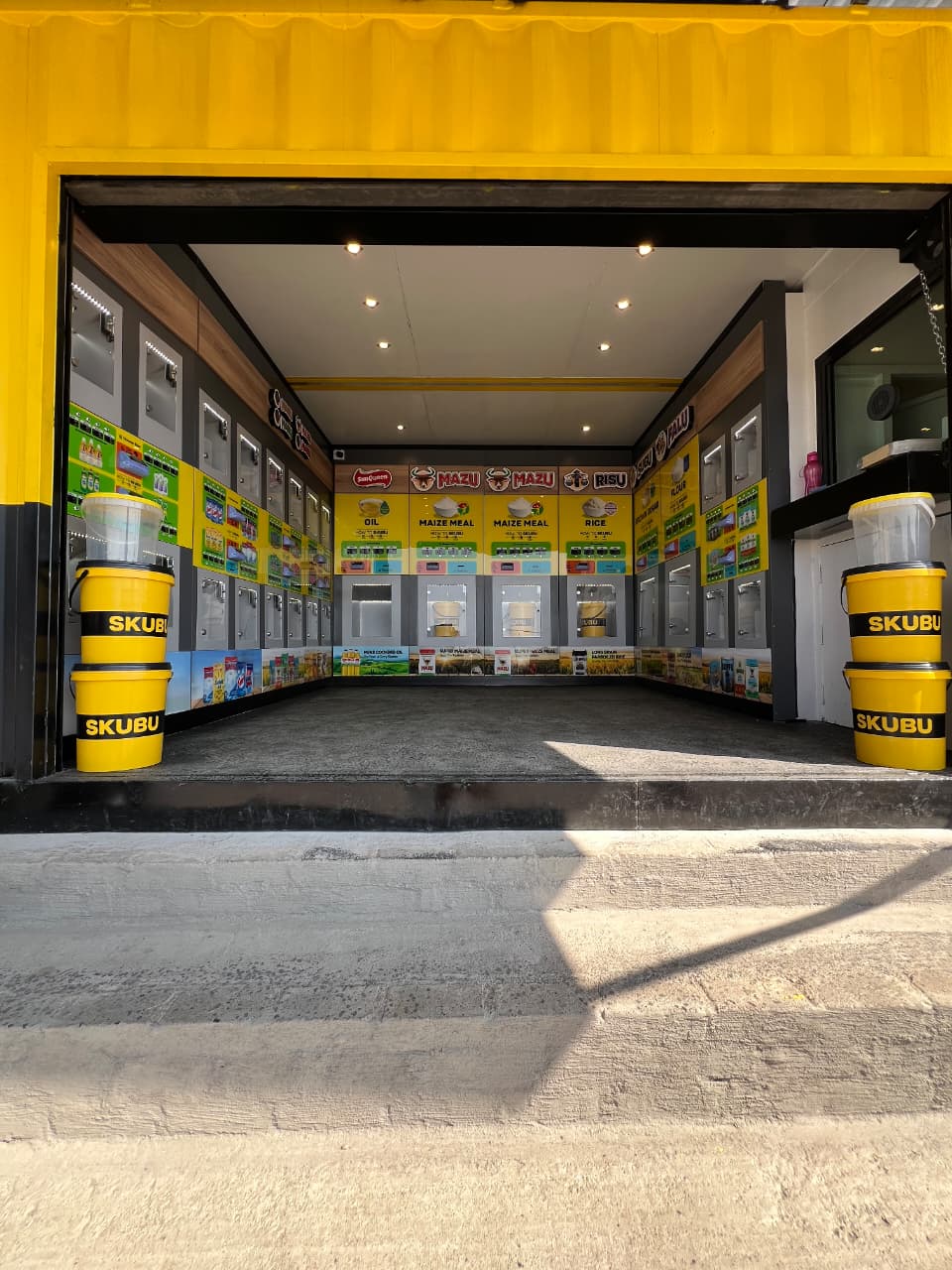 Inside a SKUBU refill store, showing the wall of dispensing units for oil, maize meal, rice, sugar and other household staples